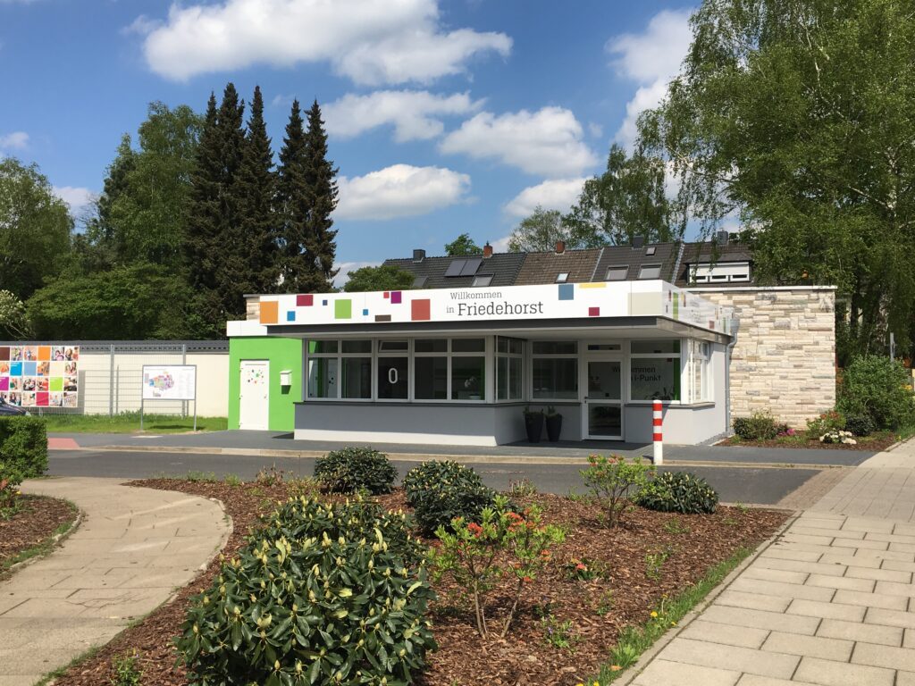 Das Empfangsgebäude der Firma Friedehorst mit der Aufschrift "Willkommen in Friedehorst". Vor dem Gebäude befinden sich gepflegte Pflanzen und ein Gehweg.