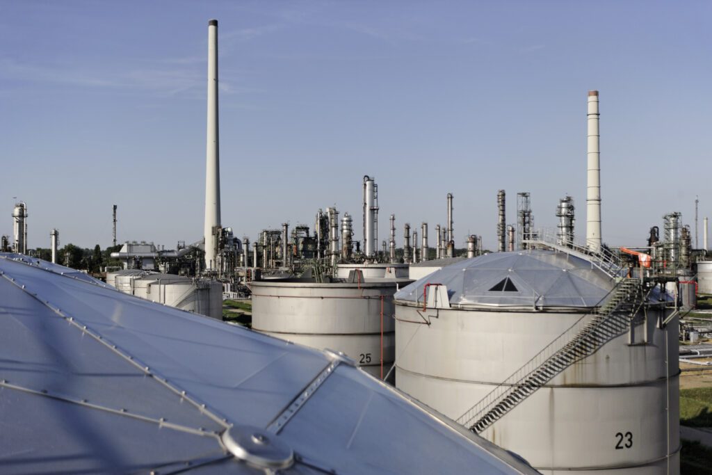 Große, silberne Lagertanks der Raffinerie Miro. Im Hintergrund sind graue Schornsteine und Rohre zu sehen.