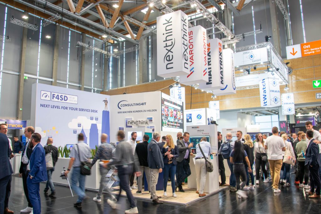 Außenansicht des Consulting4IT Standes aus einer weiter entfernten Perspektive, während viele Menschen auf und neben dem Stand unterwegs und teils in Bewegungsunschärfe zu sehen sind.