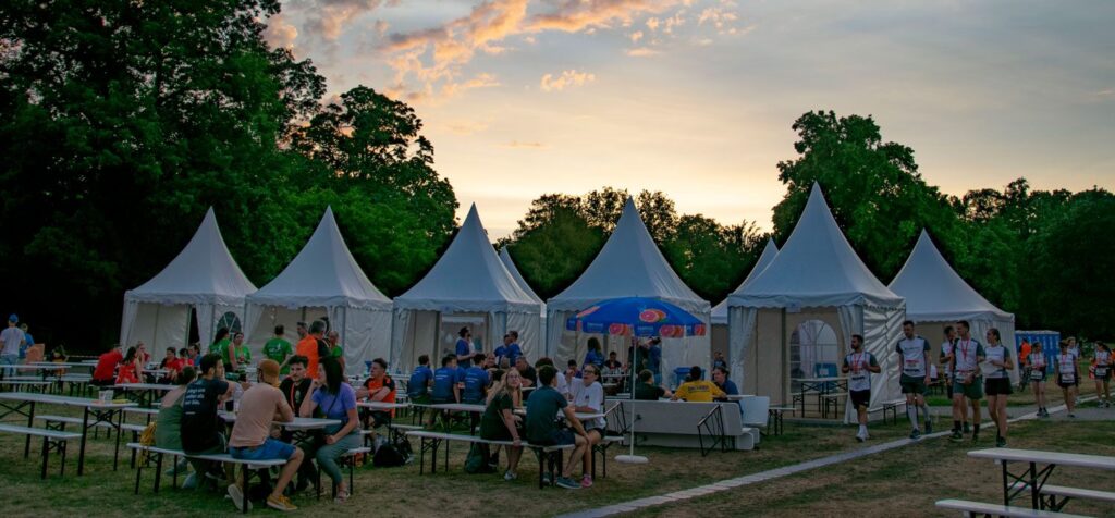 Weiße Zelte, Biertische, Bierbänke und Besucher des B2run im Karlsruher Schlossgarten bei Sonnenuntergang.