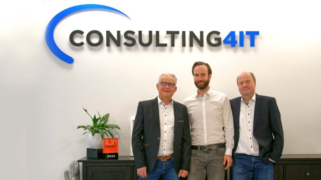 Die drei Geschäftsführer der Consulting4IT - Mirko Oesterhaus, Patrick Hild und Christian Müller - vor dem Unternehmenslogo.