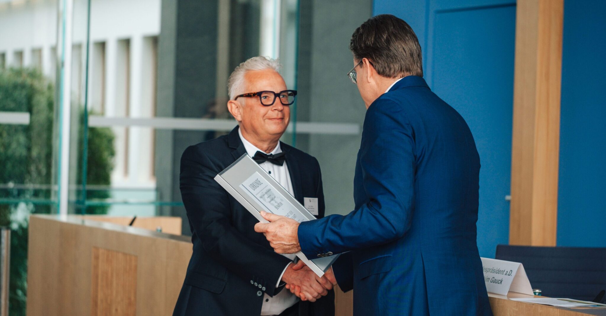 Ein Mann überreicht Mirko Oesterhaus, Geschäftsführer der Consulting4IT GmbH, bei einer offiziellen Veranstaltung die Urkunde zum Senator.