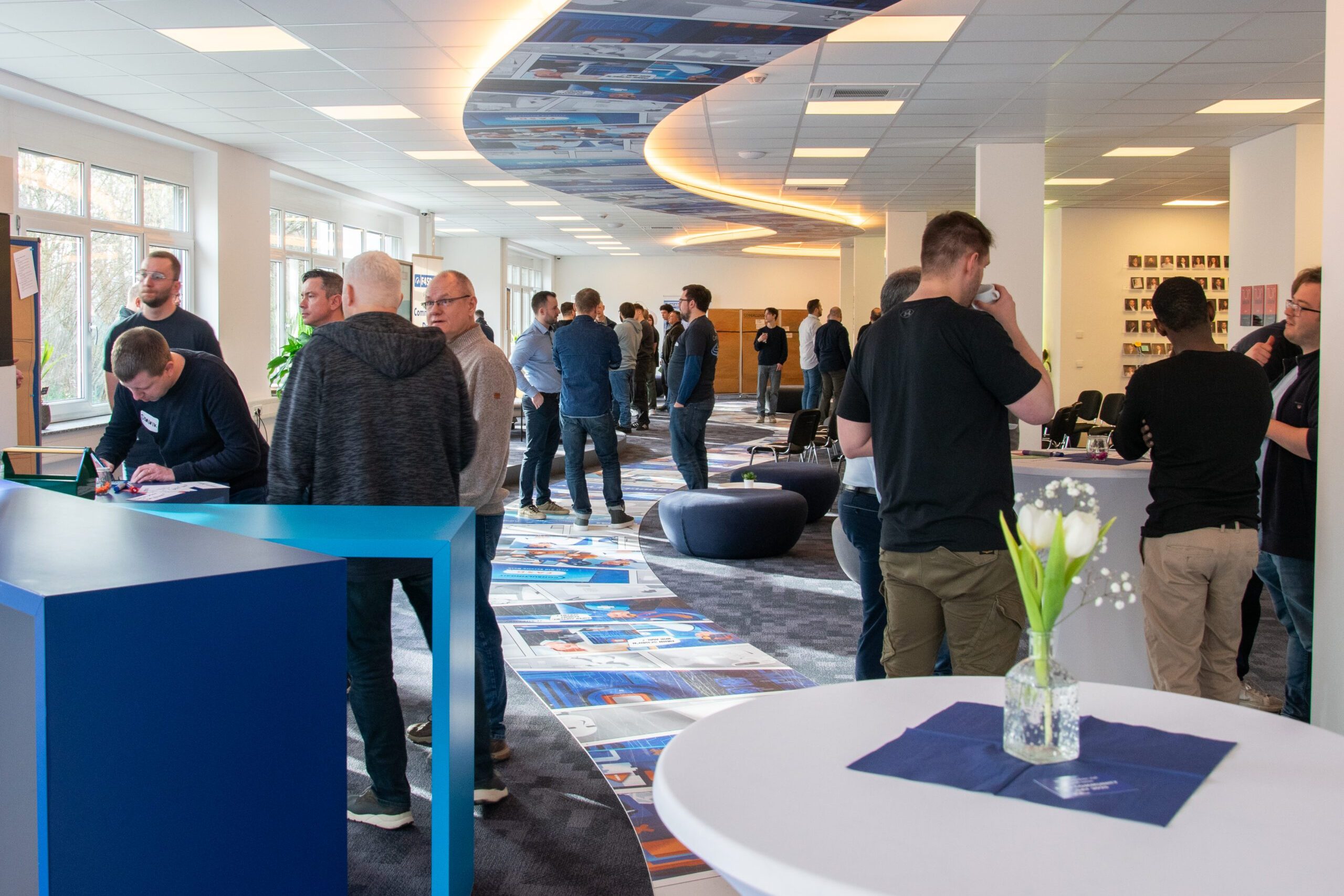 F4SD Community Day_2025 Offene Networking-Session in einem modernen Veranstaltungsraum mit vielen Teilnehmenden im Gespräch. Im Vordergrund ein runder Stehtisch mit Blumendeko, im Hintergrund lockere Gruppen und Infowände.